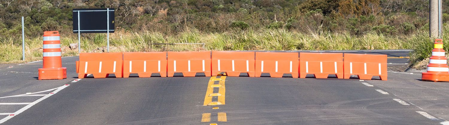 A row of orange road barriers blocks a roadway, preventing vehicles from passing.