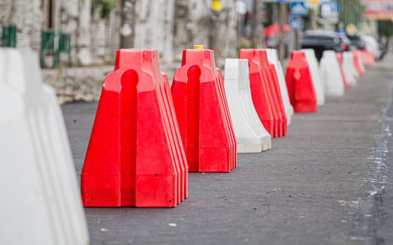 Red and white road barriers sit on a road, preventing vehicles from passing.