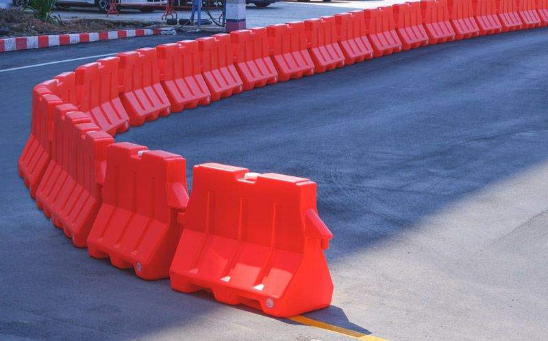 A row of orange jersey barriers sits curved on an asphalt road.